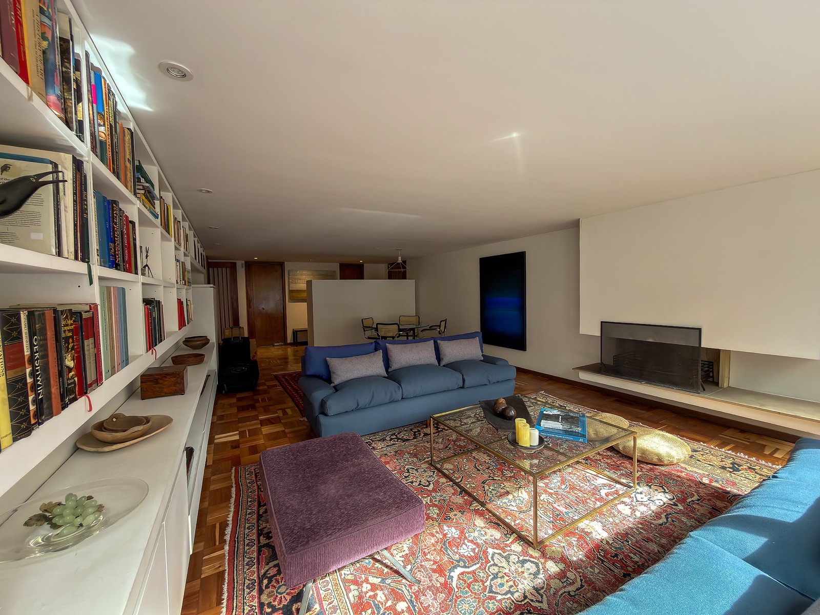 Sala amplia con biblioteca empotrada, sofás azules, tapete estampado y chimenea