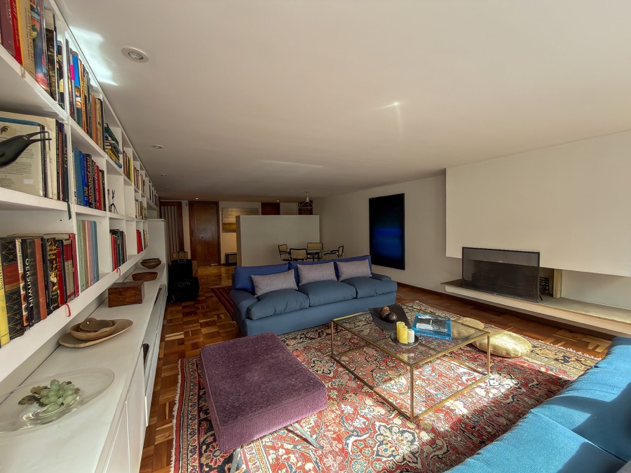 Sala amplia con biblioteca empotrada, sofás azules, tapete estampado y chimenea